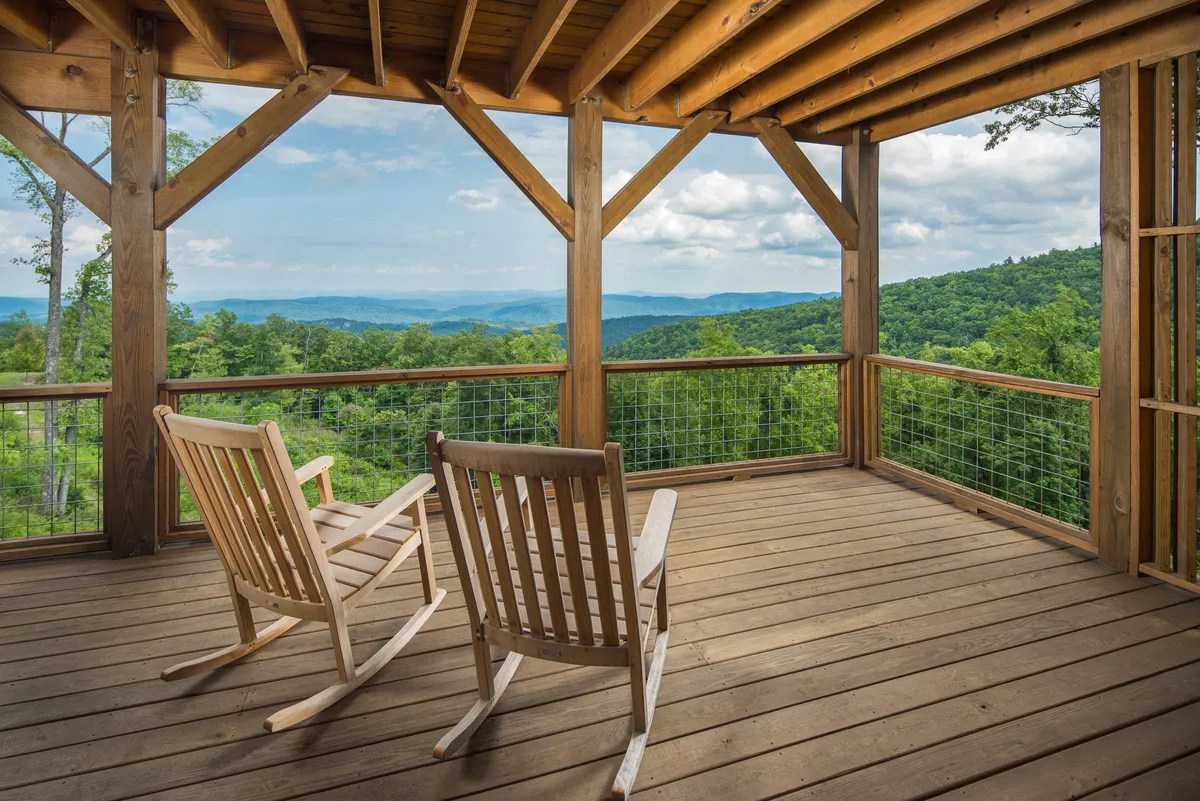 A porch with rustic rocking chairs and wooden beams overlooking a sweeping mountain view, ideal for sunrise watching or evening relaxation. The scene is tranquil and directly connects the home to the surrounding wilderness.