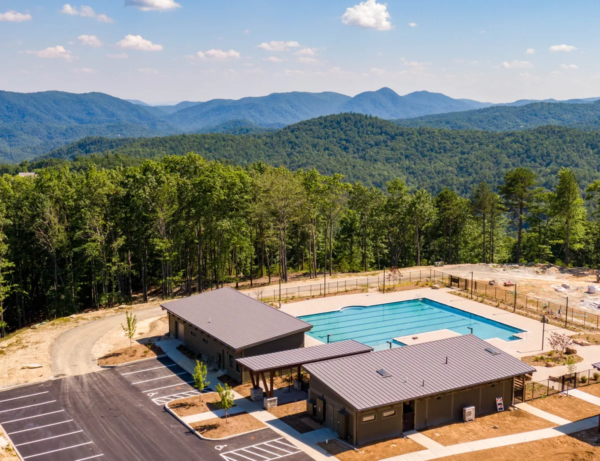 A sparkling swimming pool sits front and center, surrounded by the beauty of the mountains and recreational buildings. The scene exudes a relaxed atmosphere, hinting at sunny swims, community events, and serene moments by the water.
