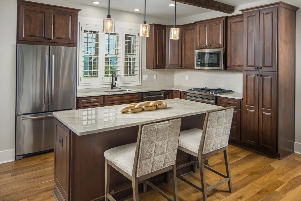 A close-up look at the modern kitchen, featuring a spacious island, stainless steel appliances, and inviting pendant lighting. A window with shutters brings in natural light and hints at the home’s thoughtful design for gatherings and meal preparation.