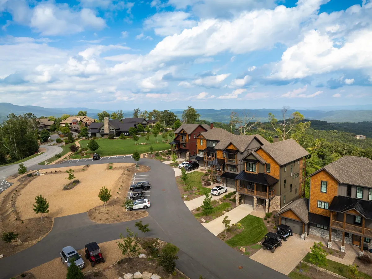 A welcoming exterior shot showing wooden architecture, green lawns, and dramatic mountain views, with a driveway and community paths inviting exploration. The scene captures the spirit of outdoor activity and community living.