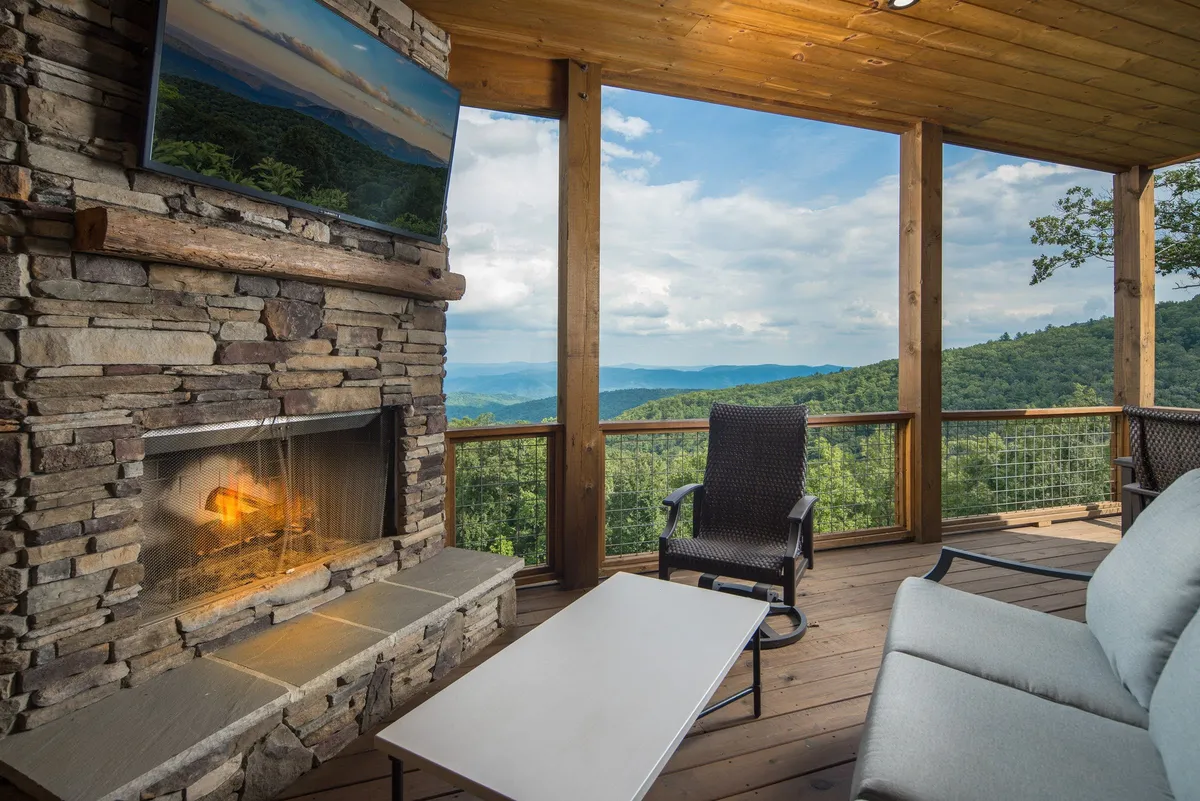 A covered patio complete with a stone fireplace, comfortable outdoor seating, and a mounted television, all with a stunning mountain backdrop. The space is designed for cozy evenings by the fire, game nights, and stargazing, highlighting year-round enjoyment.