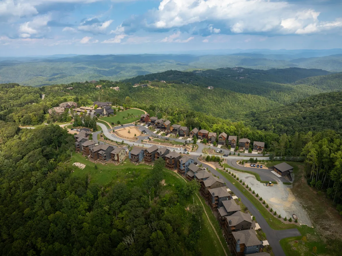 A wide exterior shot showing a lush green lawn framed by a mountain range and residential buildings. The open space invites outdoor activity and connection with nature, set against a serene, expansive view.